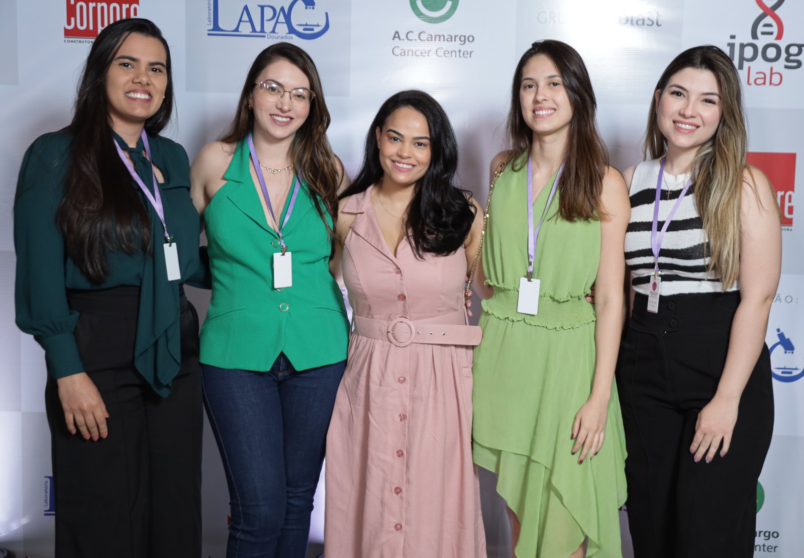 Cinco participantes com crachá em frente ao painel com as marcas do LAPAC e do IPOG Lab