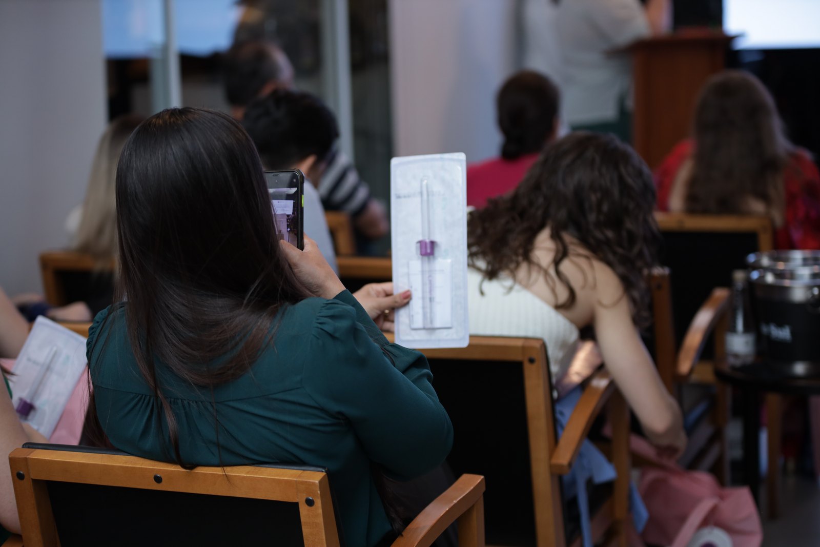 Participante na plateia segura um dispositivo de coleta embalado durante uma palestra