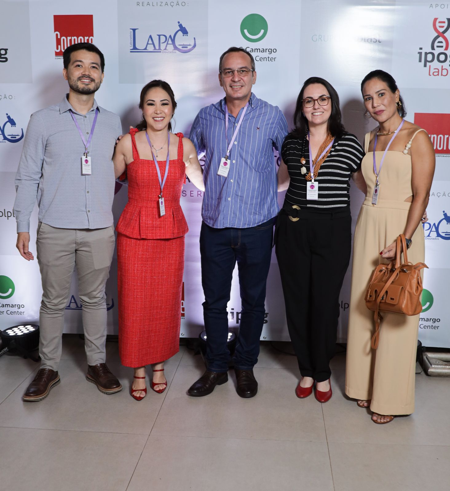 Cinco participantes em frente ao painel do simpósio, no espaço do evento