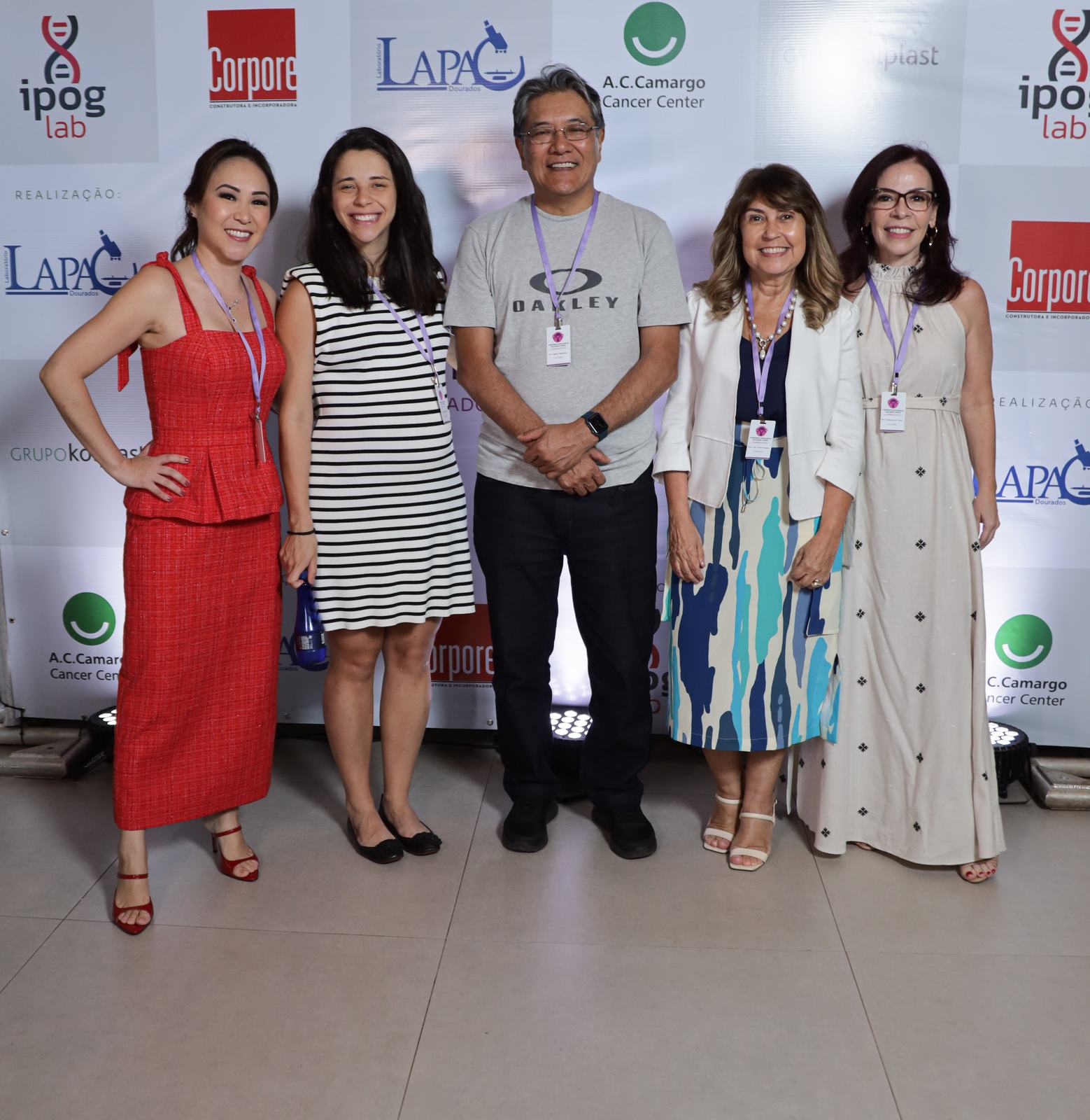 Grupo de cinco participantes sorridentes, com crachá, em frente ao painel do simpósio