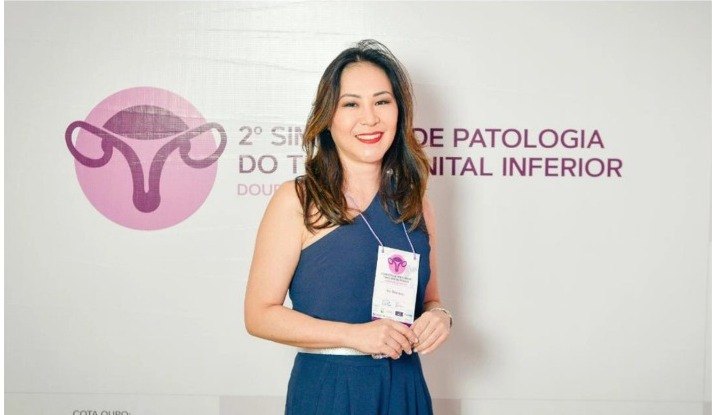Participante de vestido azul-marinho, com crachá, em frente ao painel do 2º Simpósio