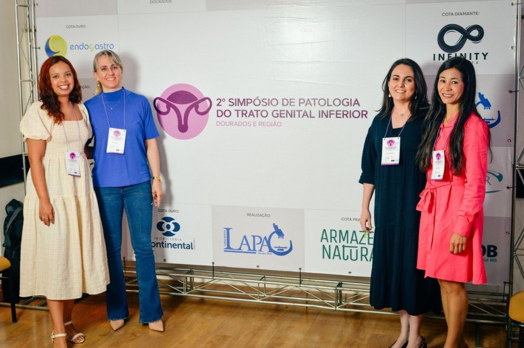 Quatro participantes em frente ao painel do 2º Simpósio, com as marcas dos apoiadores